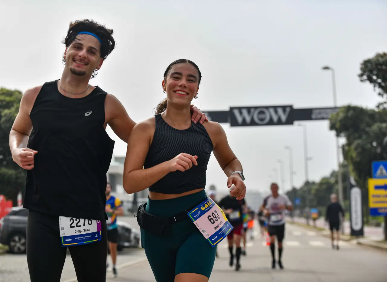 Dois corredores sorriem lado a lado, sob o pórtico WOW da prova.