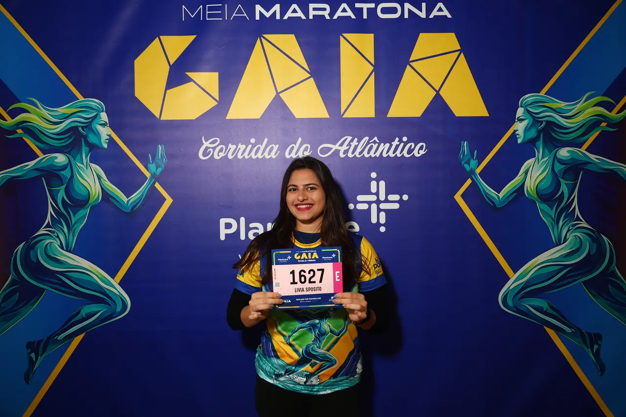Participante posa com o dorsal junto ao painel oficial da prova.