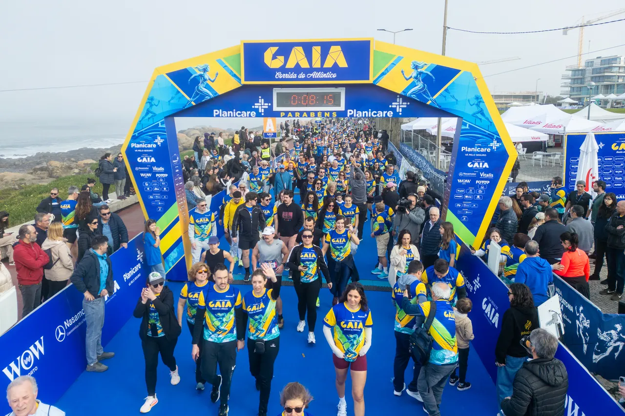Centenas de participantes na Meia Maratona de Gaia avançam pela marginal em direção ao arco de meta, com o oceano Atlântico à esquerda.