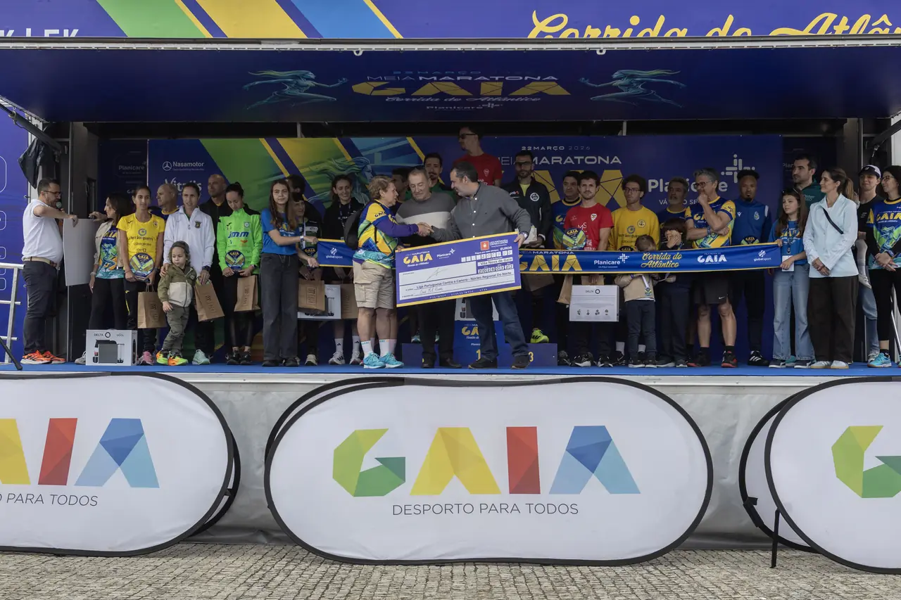 A entrega do cheque à Liga Portuguesa Contra o Cancro no palco da meta em 2026, com a organização, os parceiros e os participantes em redor.