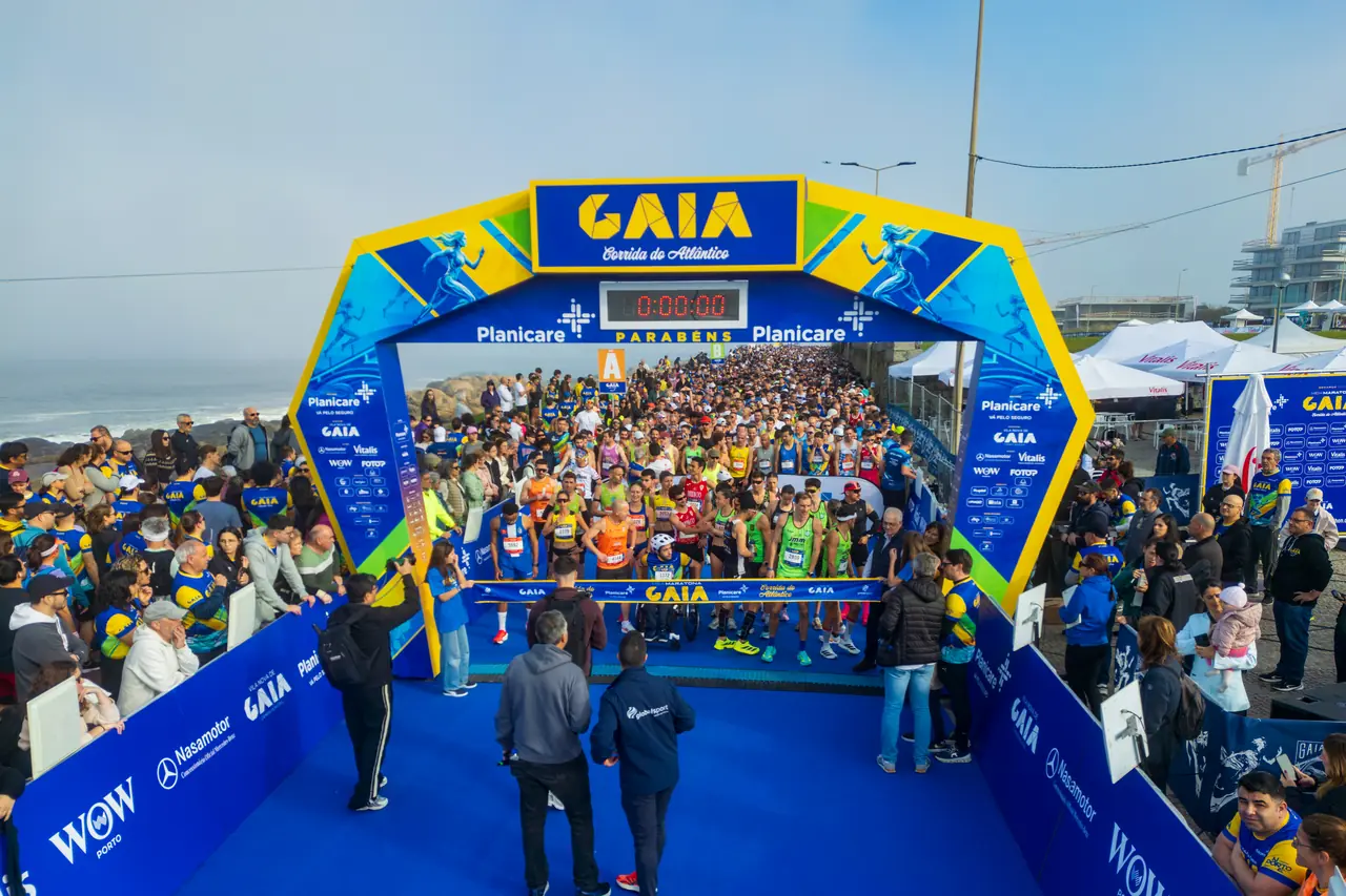 A largada da Meia Maratona de Gaia 2026 vista de frente: o pelotão inteiro atrás do arco de partida, com o público encostado às barreiras dos dois lados.