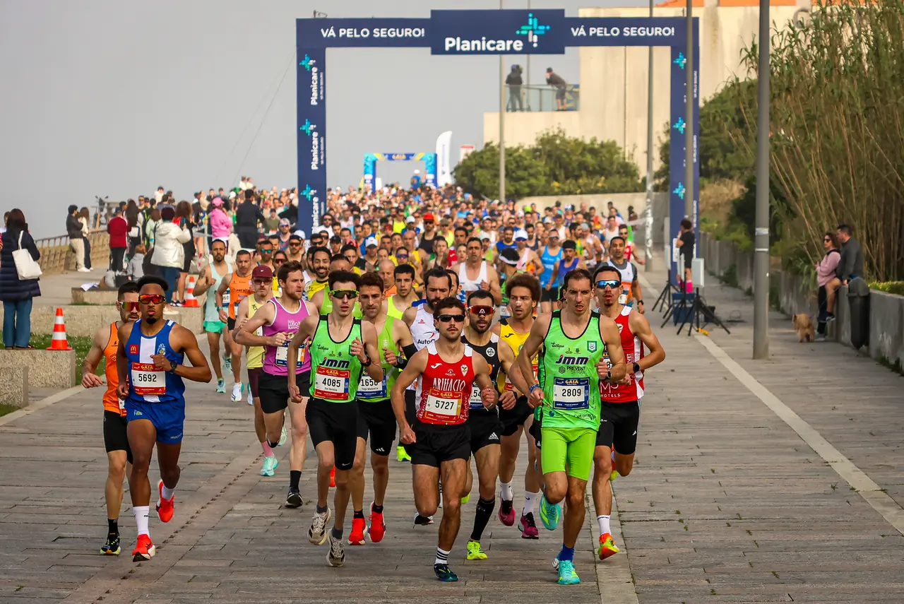 O pelotão da frente dos 21 quilómetros a correr na marginal de Gaia em 2026, sob o pórtico do patrocinador principal, com o oceano à esquerda.